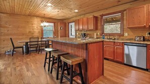 Ein Holzblockhaus-Innenraum mit Küchenbereich, inklusive Bar, Hockstühlen, Holzschränken und Geschirrspüler.