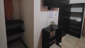 Habitació amb un televisor penjat a la paret, un escriptori petit amb un ram i un armari amb mirall.