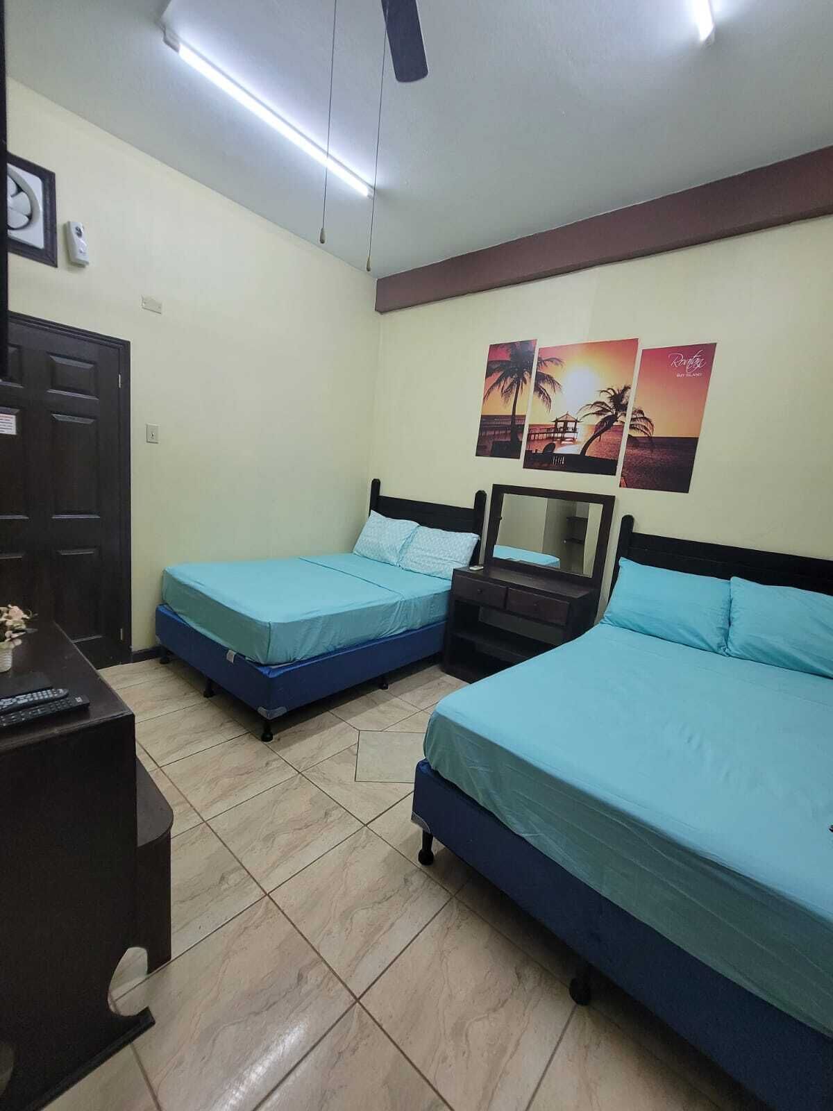 Una habitación con dos camas, un escritorio, una silla, un ventilador de techo y una puerta.