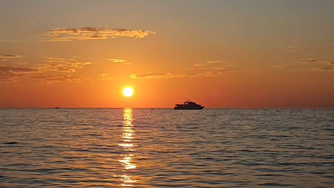 Atardecer sobre un mar tranquilo con un barco a lo lejos.