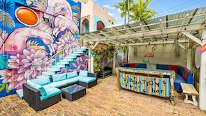 A vibrant outdoor seating area with a colorful mural, a tiki bar, and a staircase leading to an upper level. - Spacious Suite at New Yorker Hotel - Pool, Free Parking, WiFi and Coffee! (Miami)