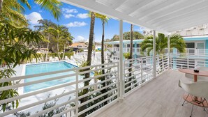 A balcony with a view of a swimming pool, palm trees, and a building in the background. - Spacious Suite at New Yorker Hotel - Pool, Free Parking, WiFi and Coffee! (Miami)