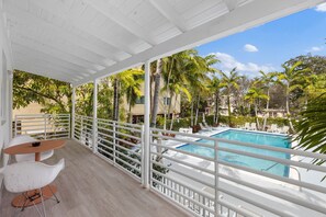 Un balcon avec une piscine, une balustrade blanche et des palmiers.