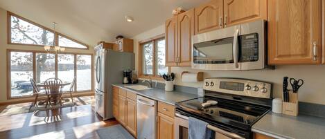 A modern kitchen with wooden cabinets, stainless steel appliances, and a large window overlooking a body of water.