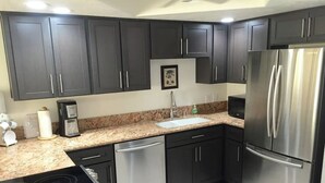 Una cocina moderna con armarios oscuros, electrodomésticos de acero inoxidable, encimera de granito y lavavajillas integrado.