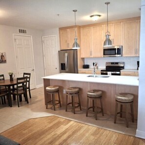 A modern kitchen with wooden cabinets, stainless steel appliances, and bar stools.