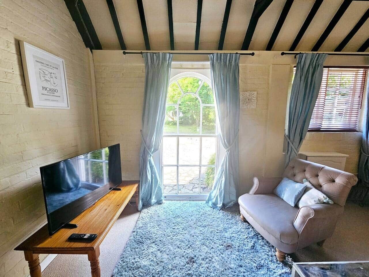 Habitació amb televisió sobre una taula de fusta, un sofà amb coixins i una finestra amb cortines.