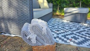 A wicker basket with a woven item on a patterned mat, a gray woven chair, and a gray sofa with cushions in an outdoor setting. - Queen Anne Cottage (Guildford)