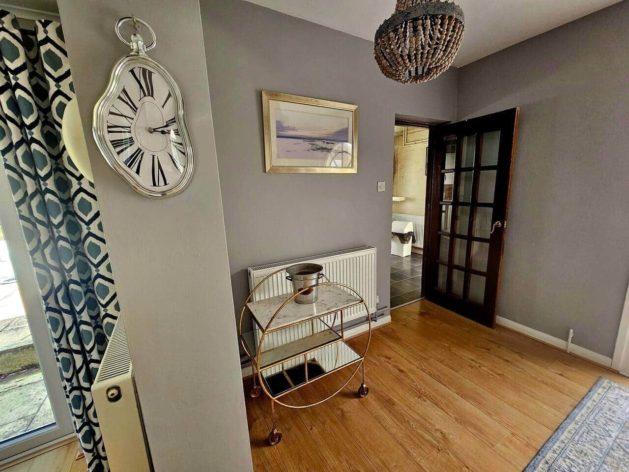 A hallway with a metal cart, a clock, and a framed picture on the wall.