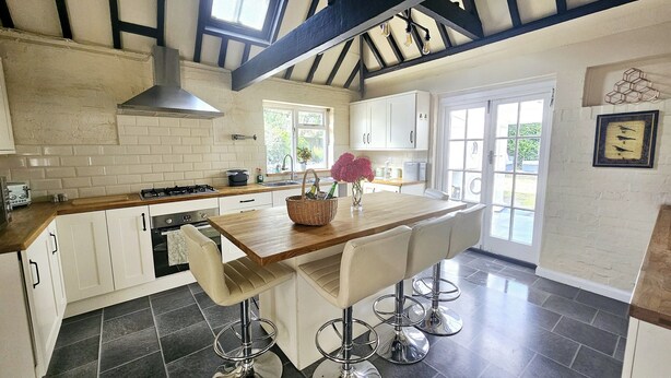 A kitchen with a central island, bar stools, and a window with natural light. - Queen Anne Cottage (Guildford)