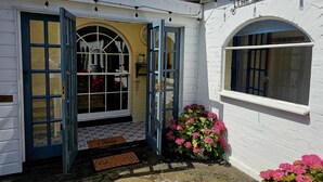 A cottage with a white exterior, a blue door, and a small porch area with a doormat. - Queen Anne Cottage (Guildford)