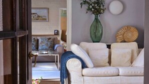 A living room with a white sofa, a green vase with flowers, and a round decorative item on the wall. - Queen Anne Cottage (Guildford)