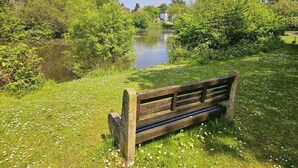 A wooden bench by a calm river surrounded by lush greenery and a clear sky. - Queen Anne Cottage (Guildford)