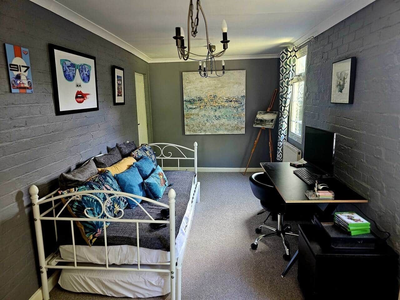 Une chambre à coucher avec un lit, un bureau, un ordinateur et des œuvres d’art accrochées aux murs.