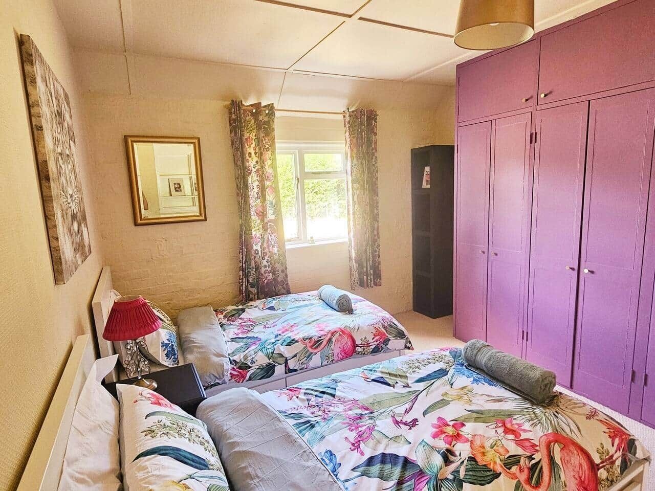 A bedroom with two beds, a wardrobe, and a window with curtains.