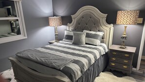 Un dormitorio con cama, dos mesitas de noche, cómoda, espejo y ventana.