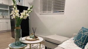 Una sala de estar moderna con un sofá, una mesita redonda con un florero, una vela decorativa y una ventana con persianas.