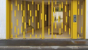 Une porte jaune avec des barreaux verticaux, le chiffre « 20 » au-dessus, et un clavier numérique sur le côté droit.