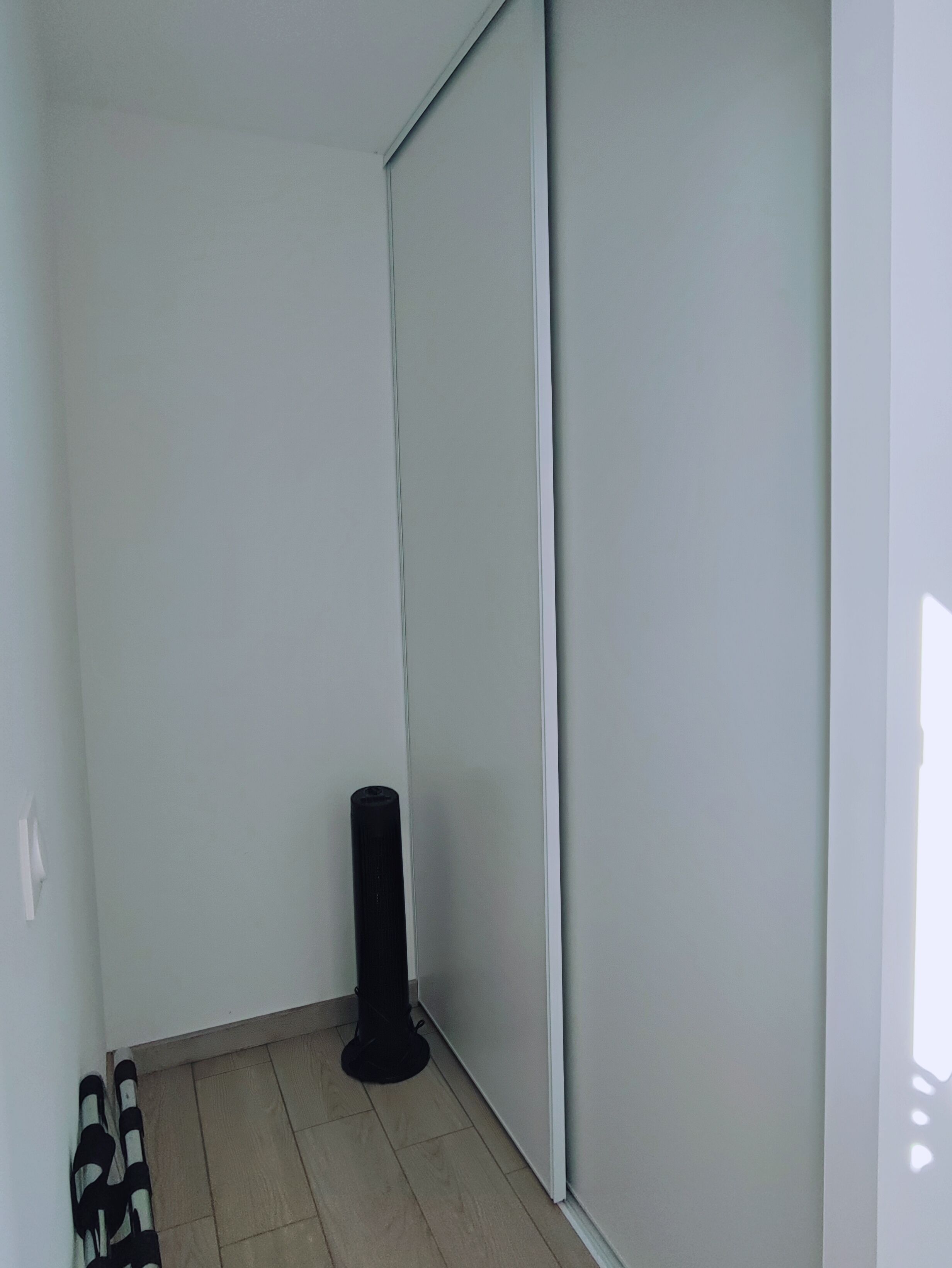 Una esquina de una habitación con una pared blanca, un objeto cilíndrico negro y un par de zapatos negros y blancos en el suelo.