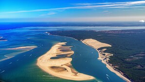 Luftaufnahme einer Küstenregion mit Sandstrand, klarem, blauem Wasser und bewaldetem Hinterland.