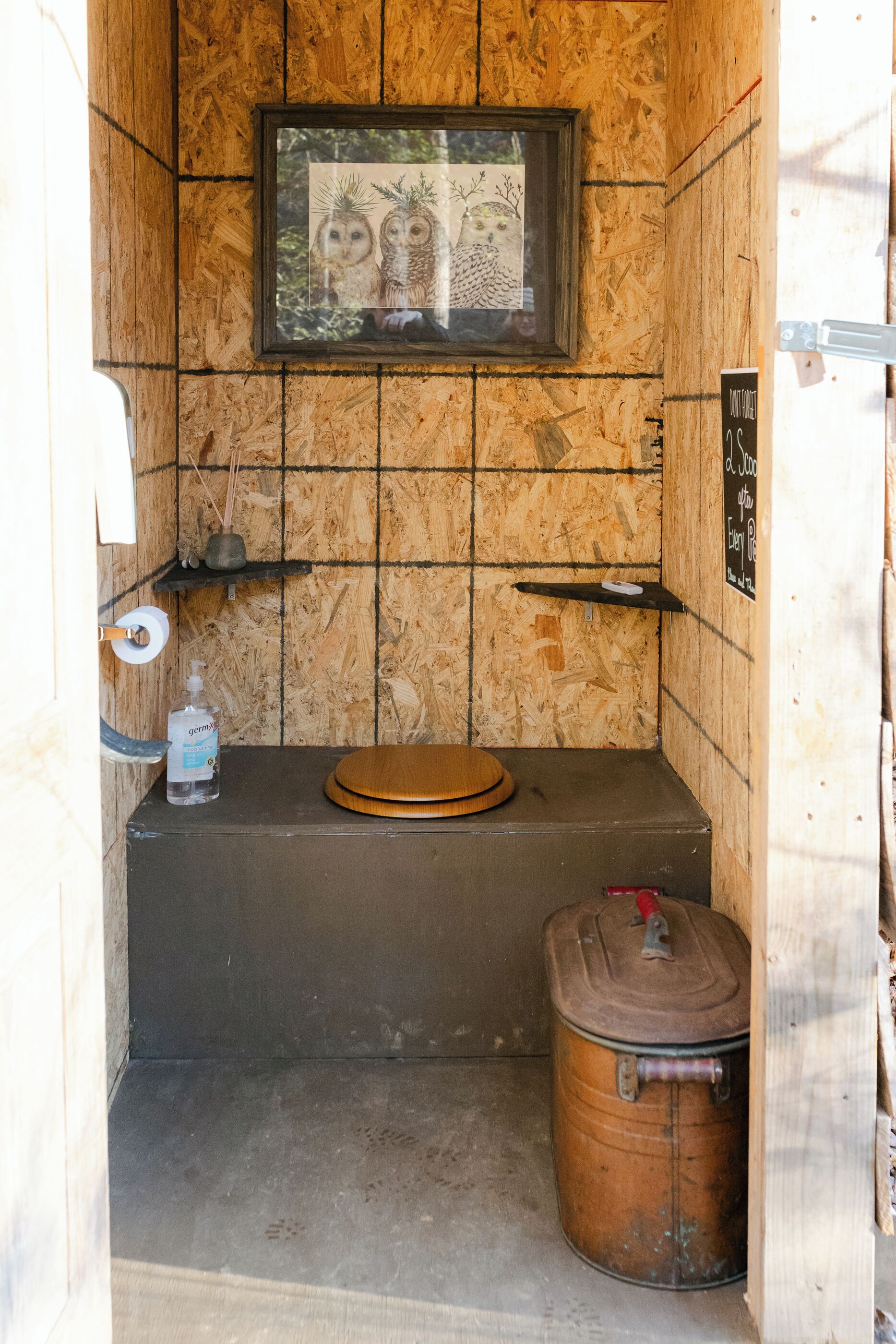 Een kleine, compacte badkamer met een houten banktoilet, een ingelijst schilderij aan de muur en een klein plankje.