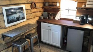 Een knus chaletinterieur met houten wanden, een kleine kitchenette, een koelkast, een koffiezetapparaat en een ingelijste foto aan de muur.