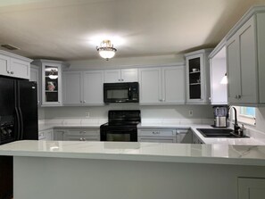 A modern kitchen with white cabinetry, a black refrigerator, a microwave, a stove, and a sink. - Peaceful family retreat-centrally located for attraction options! (Longwood)