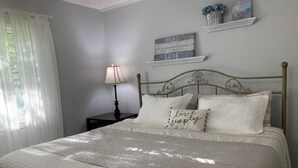 Un dormitorio con cama, mesita de noche, lámpara y objetos decorativos en la pared.