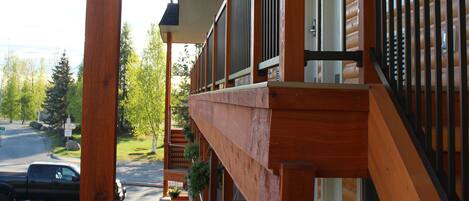 A wooden building with a balcony, a staircase, and a view of a road and trees.