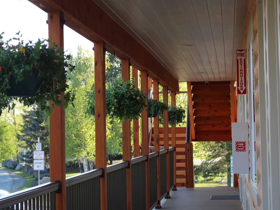 A covered wooden deck with railings and hanging plants, leading to a building entrance.