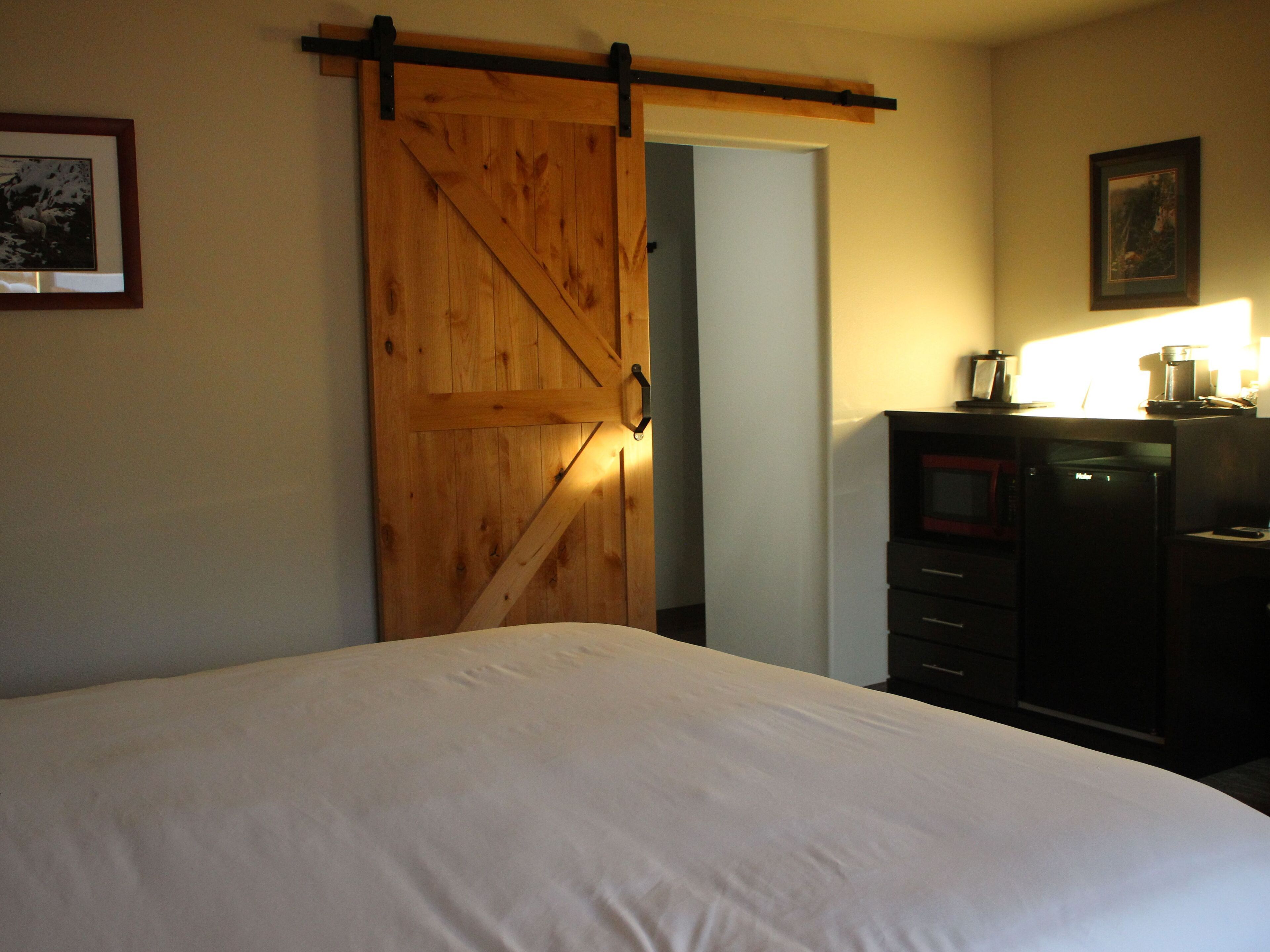 Un dormitorio con una cama, una puerta corredera de madera, un aparador y un cuadro en la pared.
