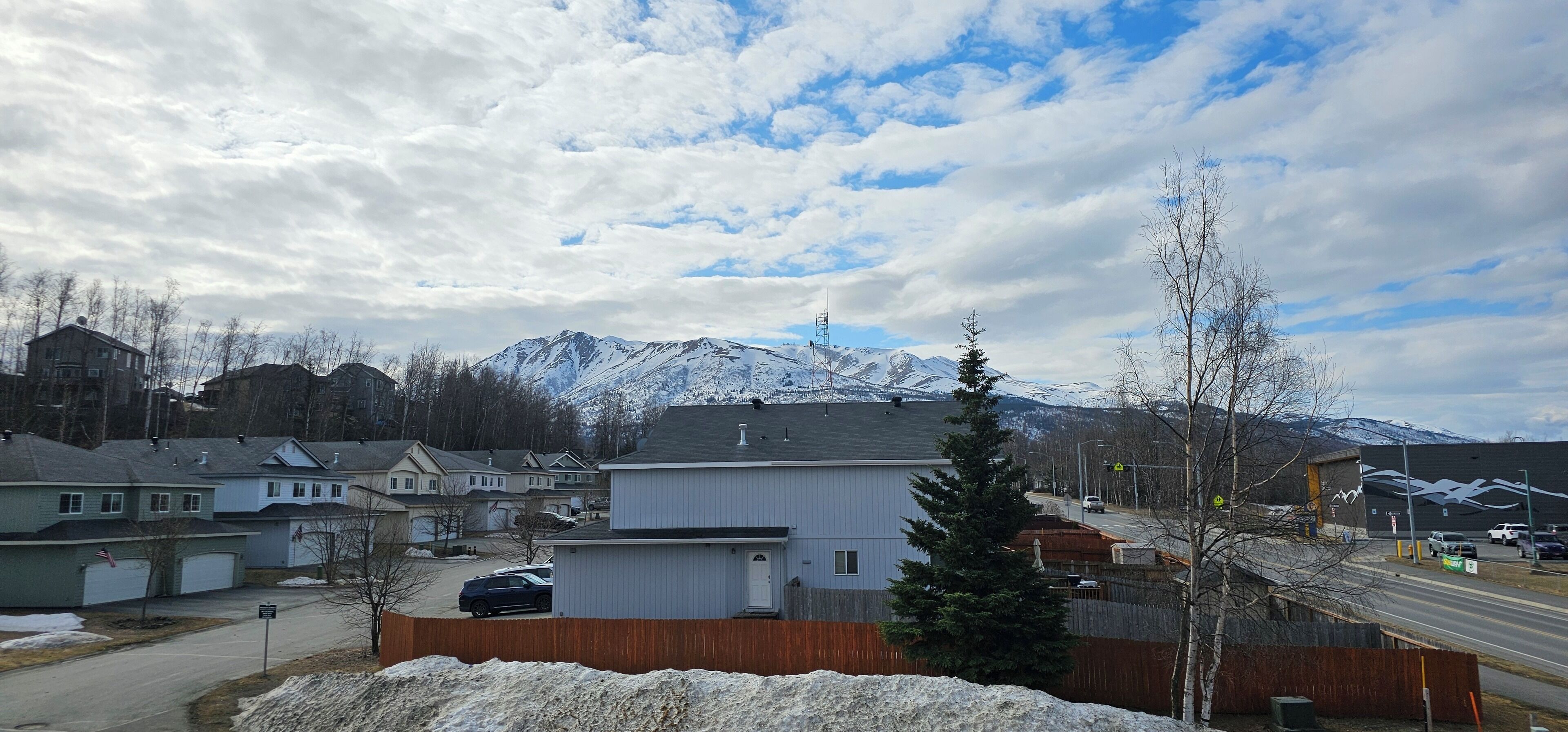 A residential area with houses, a road, and snow-covered mountains in the background.