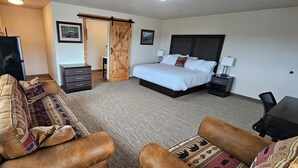 A hotel room with a bed, a sofa, a desk, a TV, and a wardrobe. - Eagle River Lodge (Eagle River)
