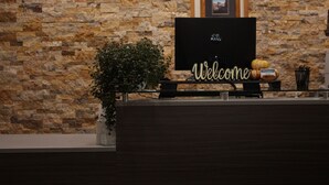A reception desk with a 'Welcome' sign, a framed picture on the wall, and a potted plant. - Eagle River Lodge (Eagle River)