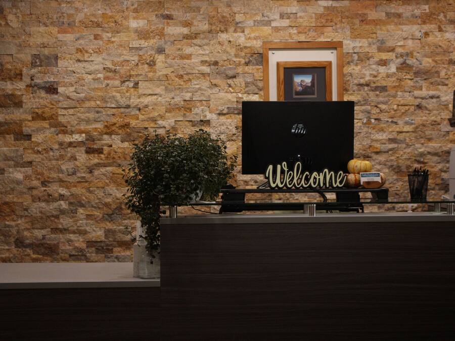 A reception desk with a 'Welcome' sign, a framed picture on the wall, and a potted plant.