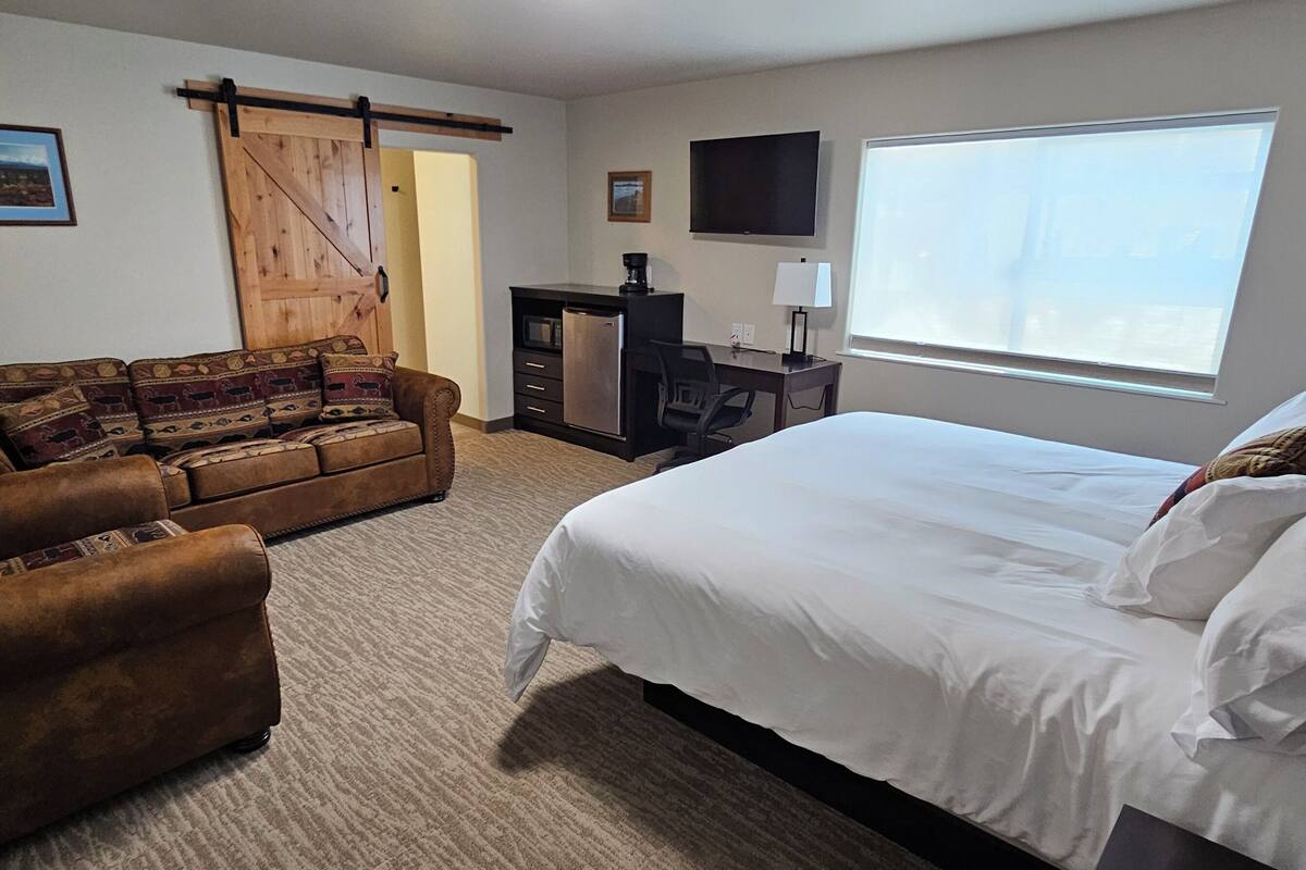 A hotel room with a large bed, a sofa, a desk with a computer, a TV, and a window with a view.