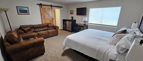 A hotel room with a large bed, a sofa, a desk with a computer, a TV, and a window with a view.