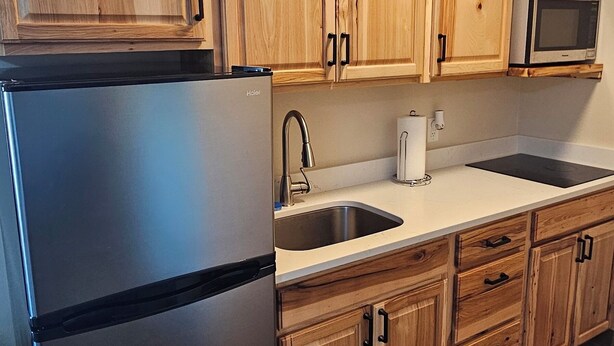 A kitchen with wooden cabinets, a stainless steel refrigerator, a microwave, and a sink. - Eagle River Lodge (Eagle River)
