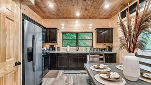 Una cocina moderna con muebles de madera, un refrigerador de acero inoxidable y un comedor con un jarrón grande y manteles individuales.