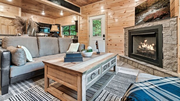 Interior acogedor de una cabaña de madera con chimenea, un sofá, una mesa de centro y una zona de cocina.