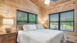 Un dormitorio de cabaña de madera con una cama, dos lámparas de noche y una mesita de noche con cajones.