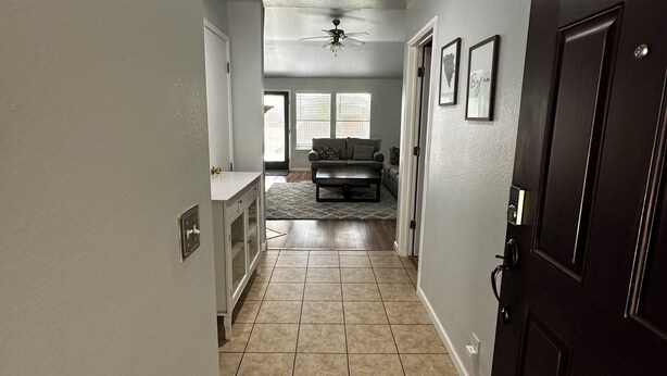 A hallway with a dark wooden door, a ceiling fan, and a window with blinds. - 3 bedroom 2 bathroom home in heart of Buda, TX. (Buda)