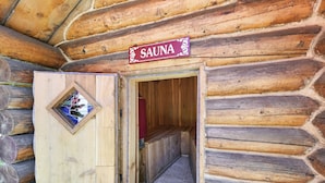 Puisesta laudeseinästä rakennettu sauna, jonka oven yläpuolella on kyltti ja ovessa pieni ikkuna.