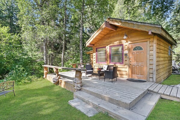 Une cabane en bois dotée d’une terrasse, de meubles de jardin et d’un escalier en pierre.