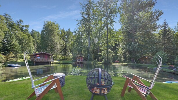 Eine Hütte am See mit Feuerstelle und zwei Stühlen.
