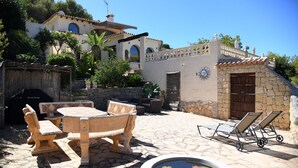 A patio with stone flooring, a wooden table and chairs, a small pool with lily pads, and a stone wall with a door. - Villa Las Viñas with swimming pool & stunning view (Teulada)