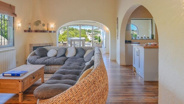 A cozy living room with a large sofa, a wooden coffee table, and a kitchen area with a dining table and chairs. - Villa Las Viñas with swimming pool & stunning view (Teulada)
