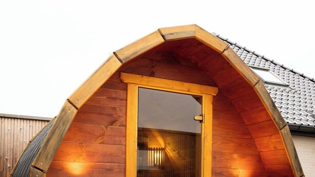 Eine Holzsauna mit Glastür, zwei Wandleuchten und einem gefliesten Boden.