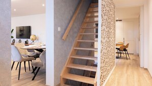 Ein modernes Interieur mit einer Holztreppe, einem Essbereich mit Stühlen und einem Tisch sowie einer Küche im Hintergrund.