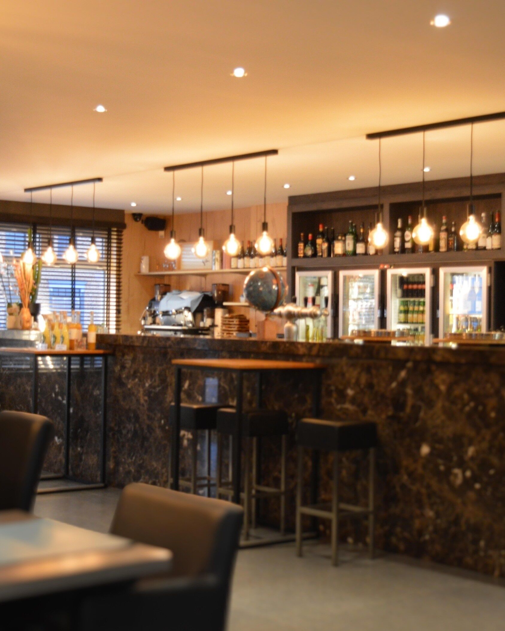 Eine Bar mit hängenden Lampen, einer Theke mit Flaschen und Sitzgelegenheiten.